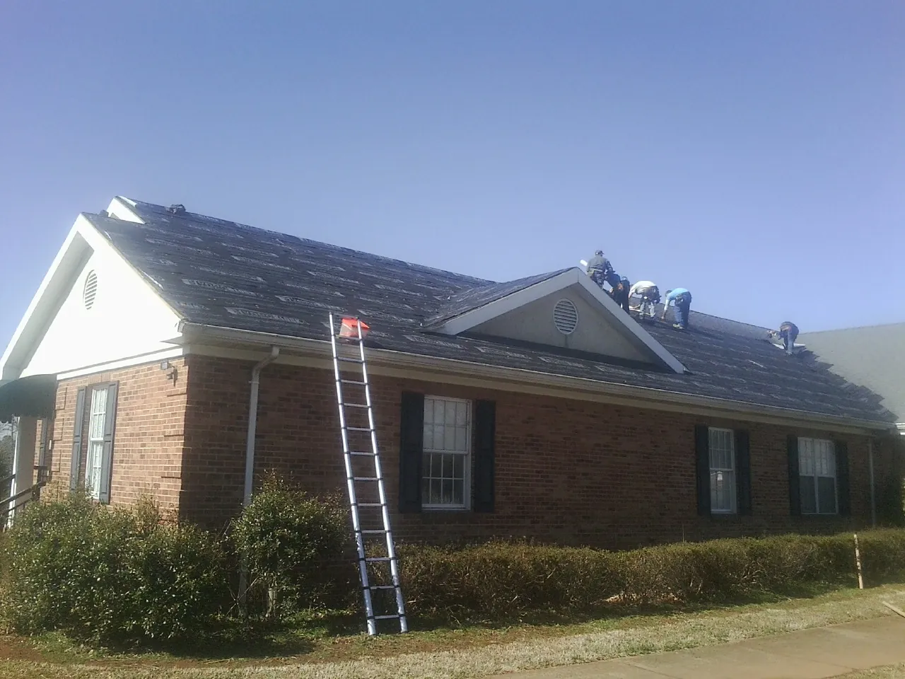 Crew tearing shingles off a brick ranch roof with a ladder set — Emergency Roof Repair work by our crew in Coats