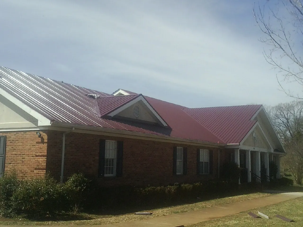 Red metal roof with gabled entries on a long brick building, from a Hail Damage Roof Repair job in Coats