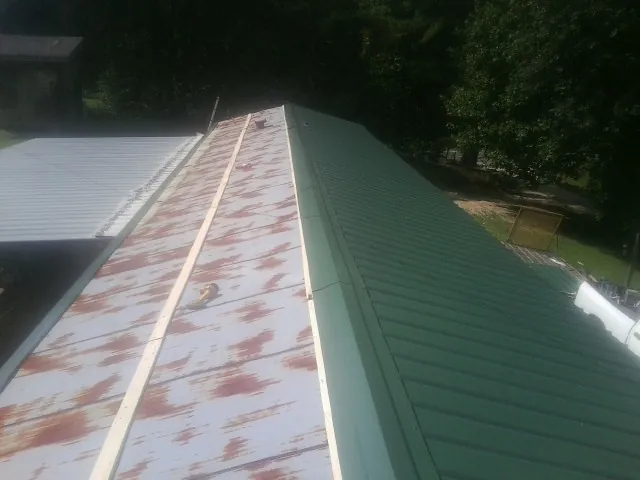 Old rusted panels beside newly installed green metal roofing — Wind Damage Roof Repair by Roofing Brothers in Coats