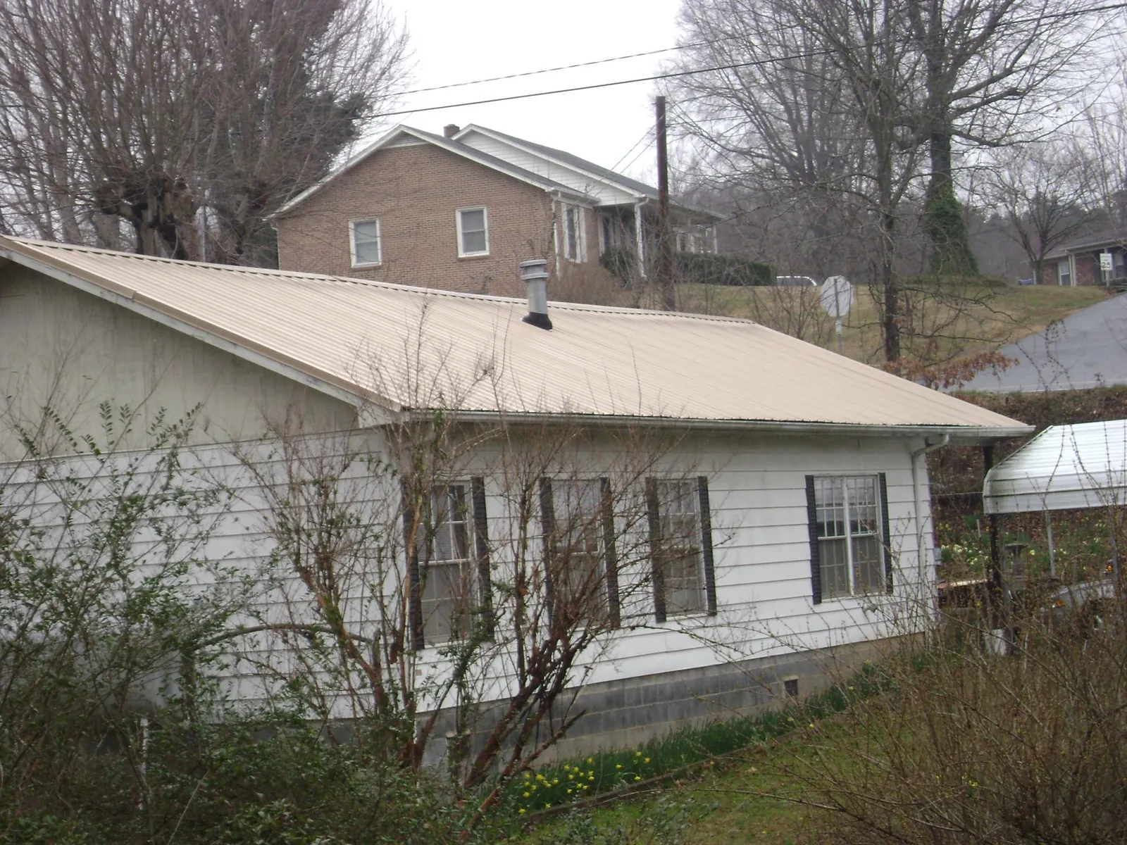 Tan metal roof on a white sided house set into a hillside — Commercial Roofing by Roofing Brothers in Coats