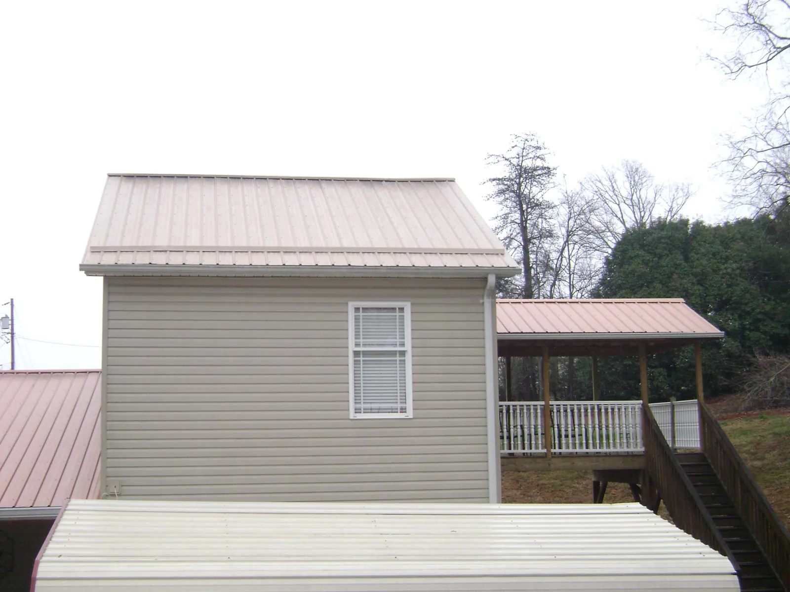 Tan metal roofs on a two story addition and attached porch, from a Roof Replacement job in Coats