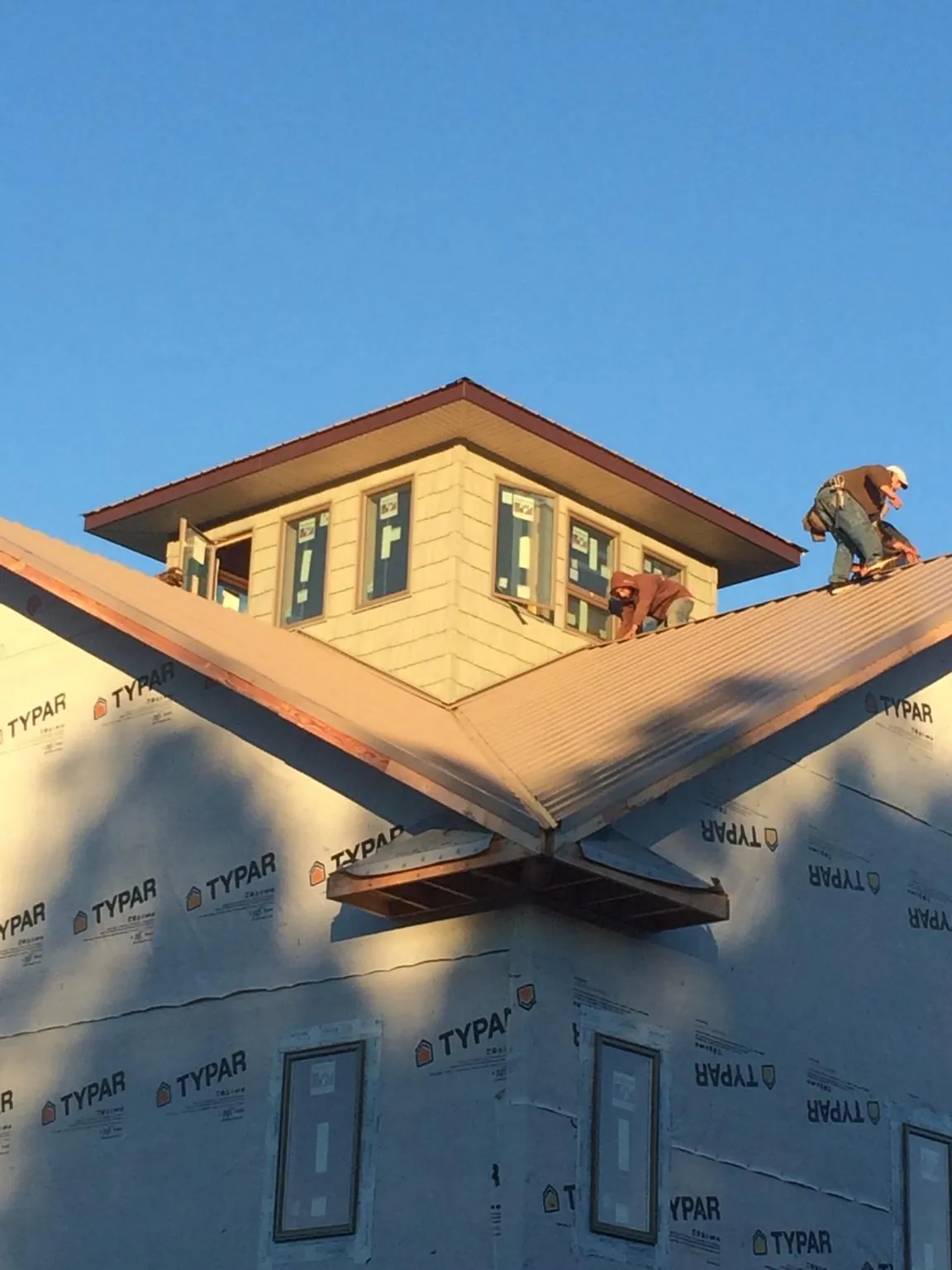 Roofers working around a rooftop cupola on a new metal roof at sunset — Roof Waterproofing in Coats by Roofing Brothers